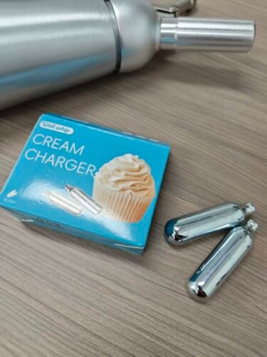Box of cream chargers with two silver N2O canisters on a light blue background.