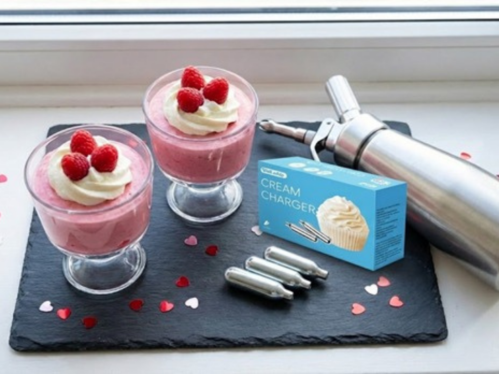 Two glasses of strawberry dessert topped with cream next to a charger box.